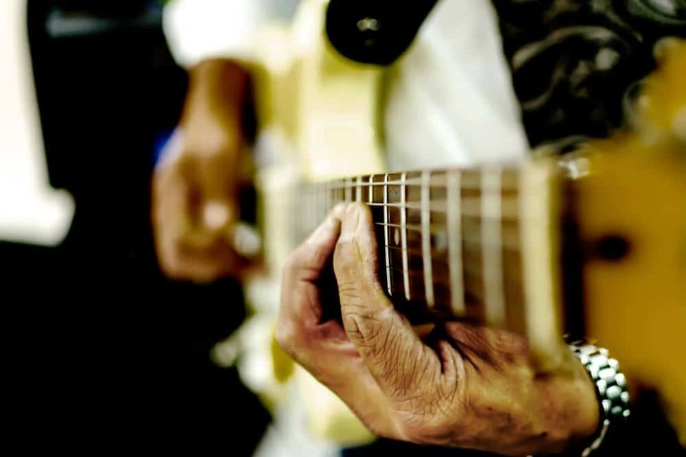 A pair of wrinkled hands playing a guitar.