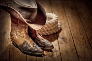 A cowboy hat and cowboy boots lay next to some rope.